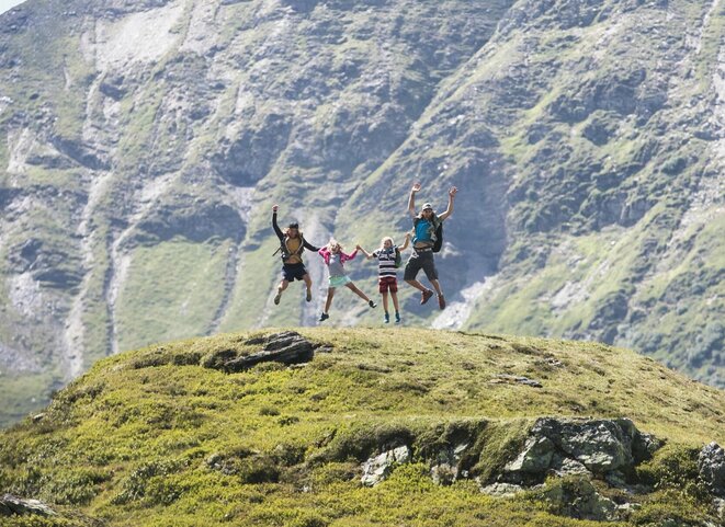 Familie macht einen Lufstsprung vor Gipfelpanorama