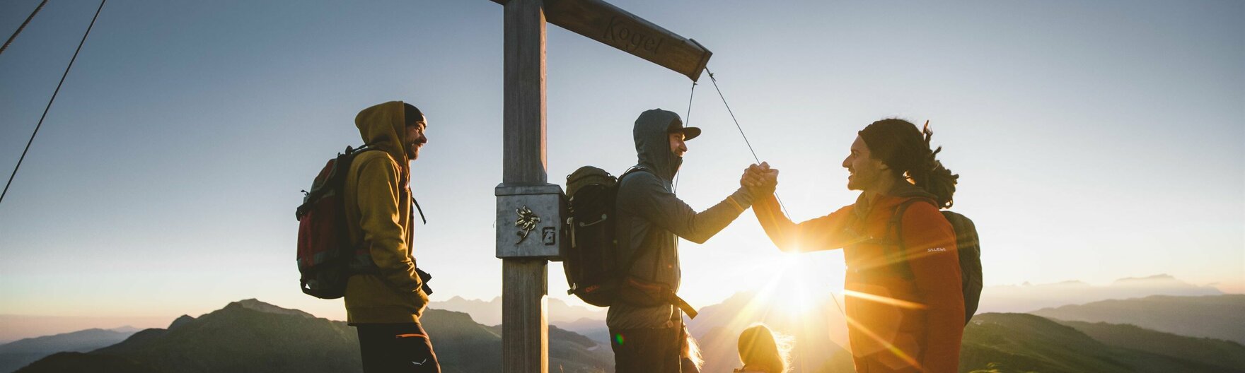 Wandergruppe bei Sonnenaufgang am Gipfelkreuz