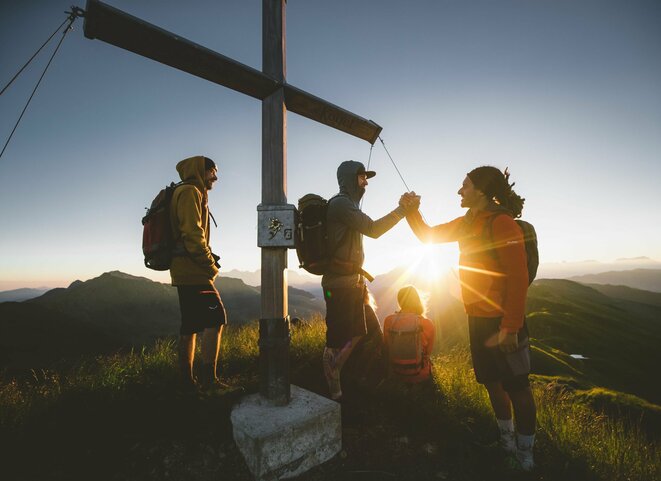 Wandergruppe bei Sonnenaufgang am Gipfelkreuz