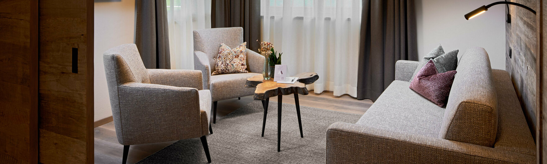 Wohnzimmer mit Sofa, 2 Sesseln, kleinem Couchtisch, Fernseher und 2 großen Fenstern im Mei.Auszeit Appartement