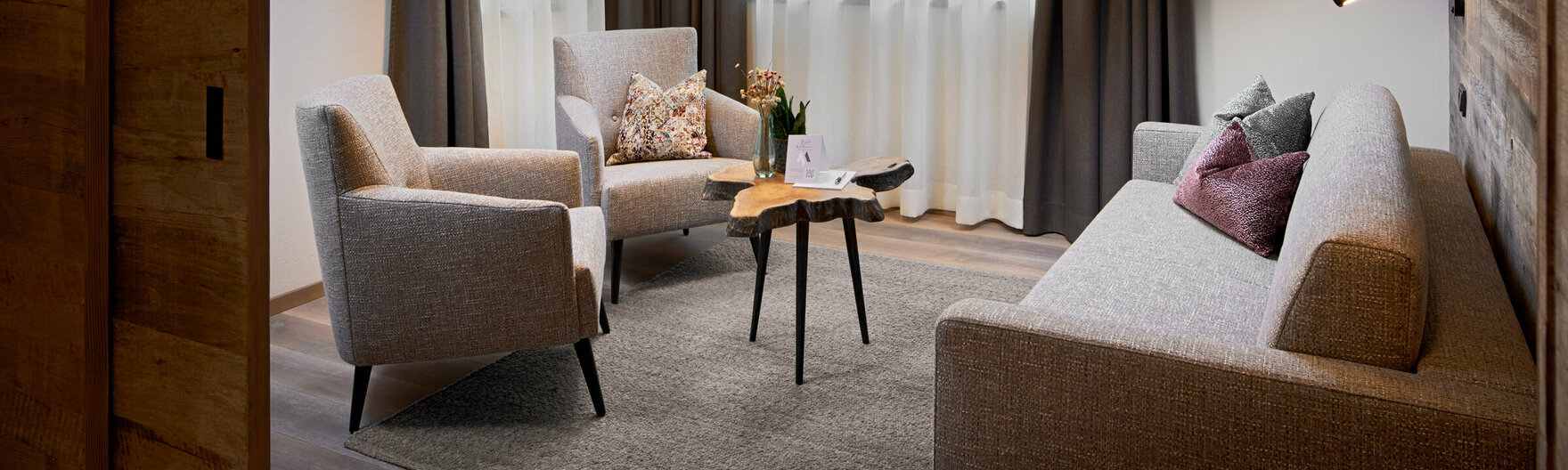 Wohnzimmer mit Sofa, 2 Sesseln, kleinem Couchtisch, Fernseher und 2 großen Fenstern im Mei.Auszeit Appartement