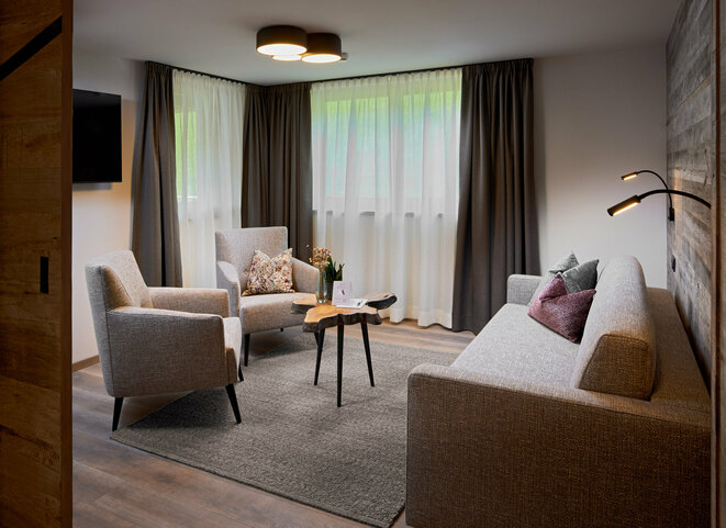 Wohnzimmer mit Sofa, 2 Sesseln, kleinem Couchtisch, Fernseher und 2 großen Fenstern im Mei.Auszeit Appartement