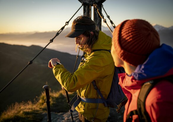 Zwei Wanderer bei Sonnenaufgang am Gipfelkreuz