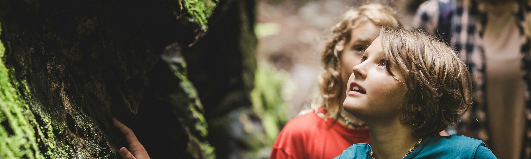 Zwei Kinder berühren moosige Felsen