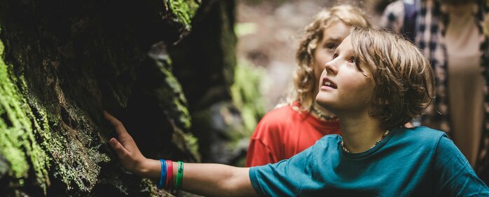 Zwei Kinder berühren moosige Felsen