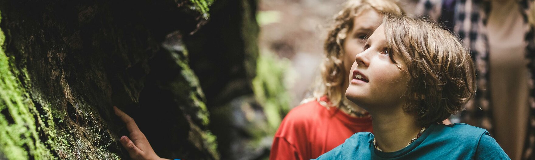 Zwei Kinder berühren moosige Felsen