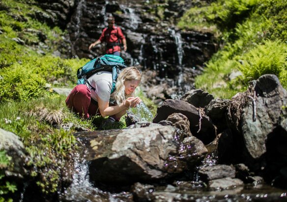 Frau trinkt klares Wasser aus Gebirgsquelle