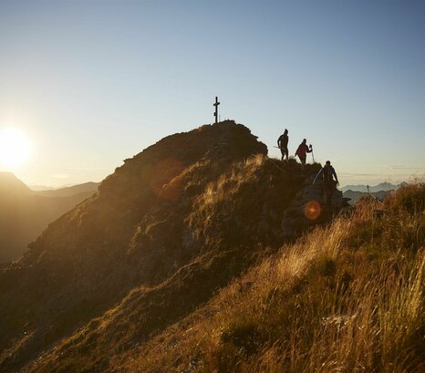 Wanderer beim Abstieg vom Gipfelkreuz bei Sonnenaufgang