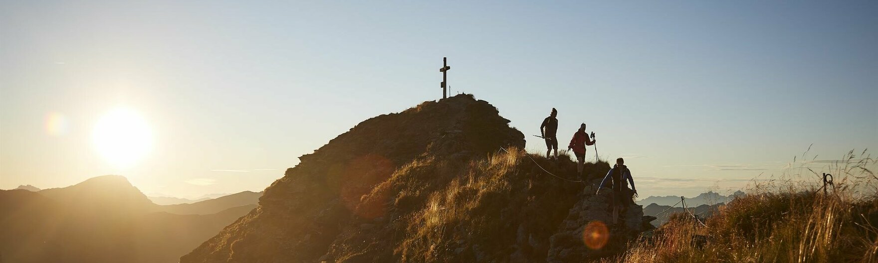 Wanderer beim Abstieg vom Gipfelkreuz bei Sonnenaufgang