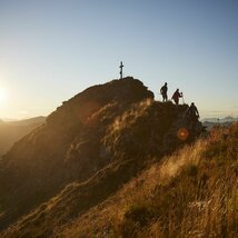 Wanderer beim Abstieg vom Gipfelkreuz bei Sonnenaufgang