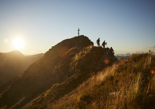 Wanderer beim Abstieg vom Gipfelkreuz bei Sonnenaufgang