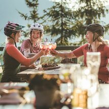 Drei Frauen in Mountainbikeausrüstung machen Rast auf der Alm