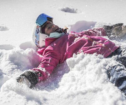 Kind mit Skiausrüstung liegt im Schnee