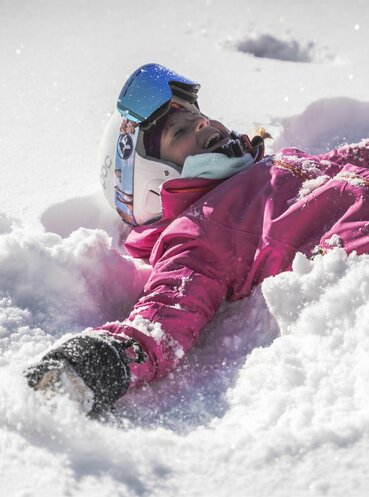 Kind mit Skiausrüstung liegt im Schnee