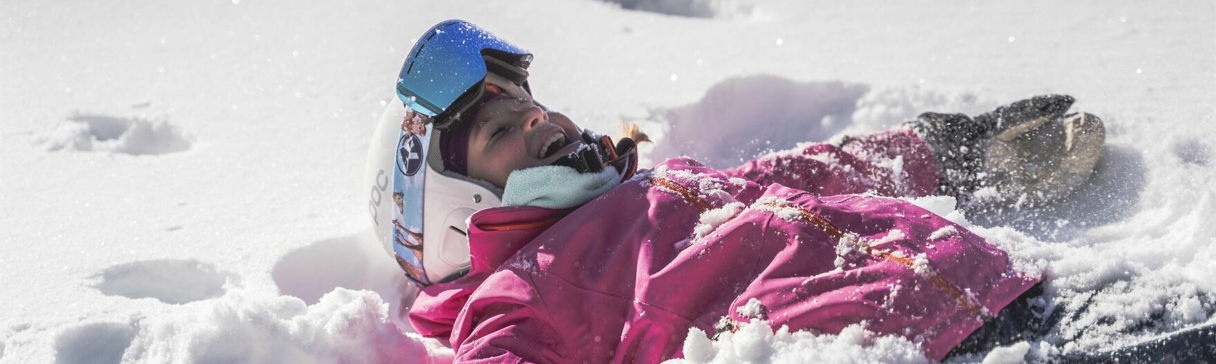 Kind mit Skiausrüstung liegt im Schnee