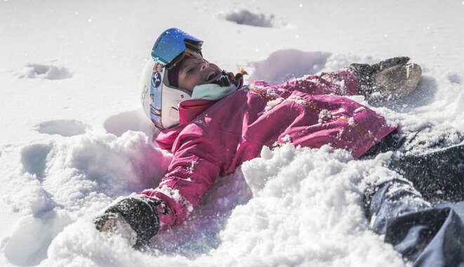 Kind mit Skiausrüstung liegt im Schnee