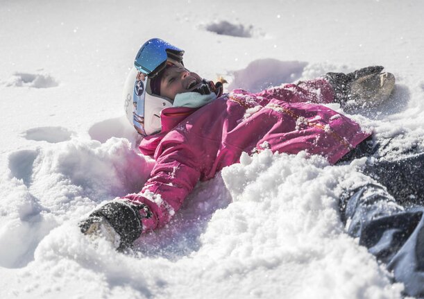 Kind mit Skiausrüstung liegt im Schnee