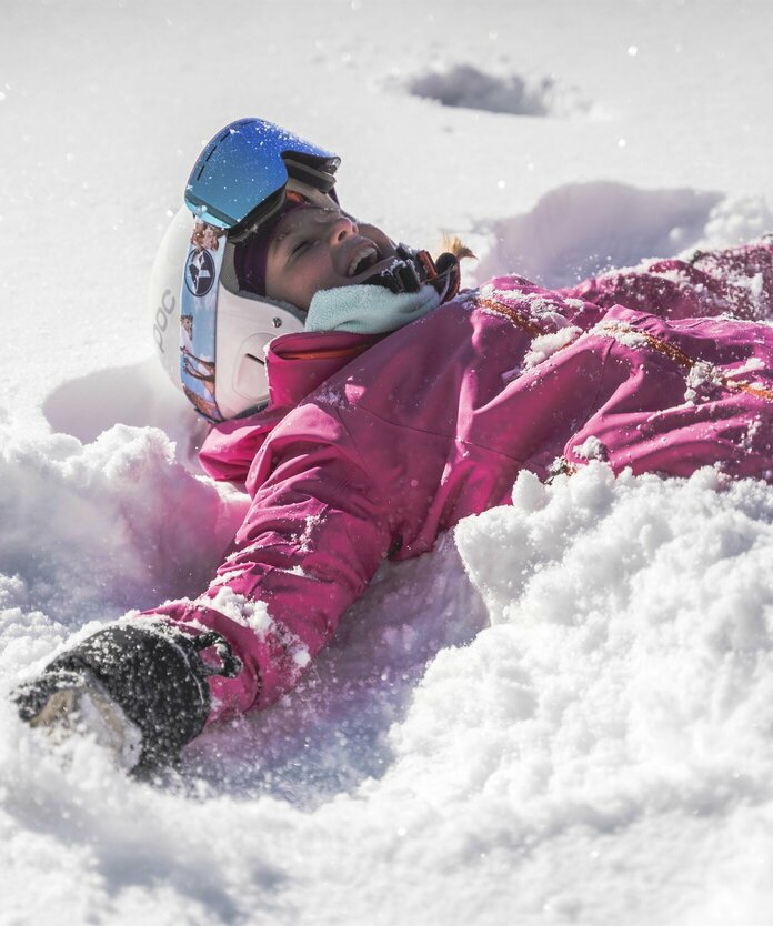 Kind mit Skiausrüstung liegt im Schnee