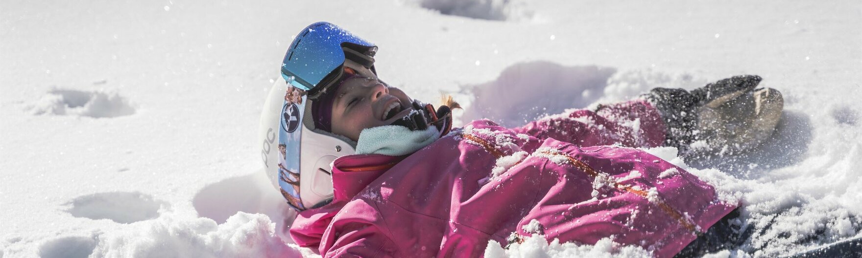 Kind mit Skiausrüstung liegt im Schnee